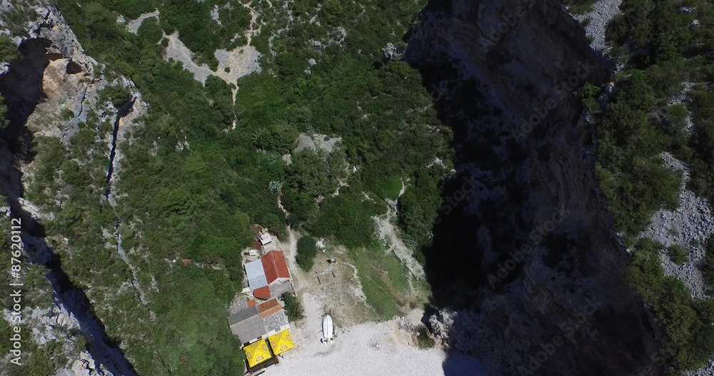 Escena aérea de bahía rocosa en costa dálmata. Dron. Acantilado rocoso sobre el agua transparente y barcos fondeados. Playa en el extremo de la bahía.