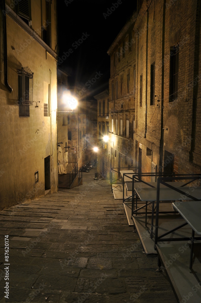 Dark narrow alley with old buildings and street lamps in Siena,Tuscany, Italy