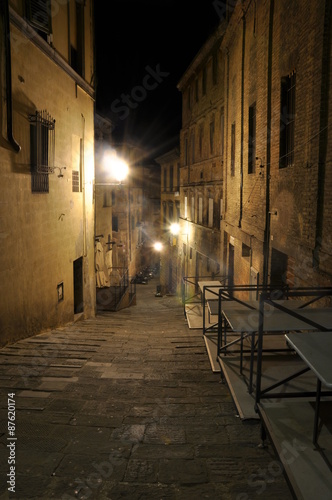 Dark narrow alley with old buildings and street lamps in Siena,Tuscany, Italy