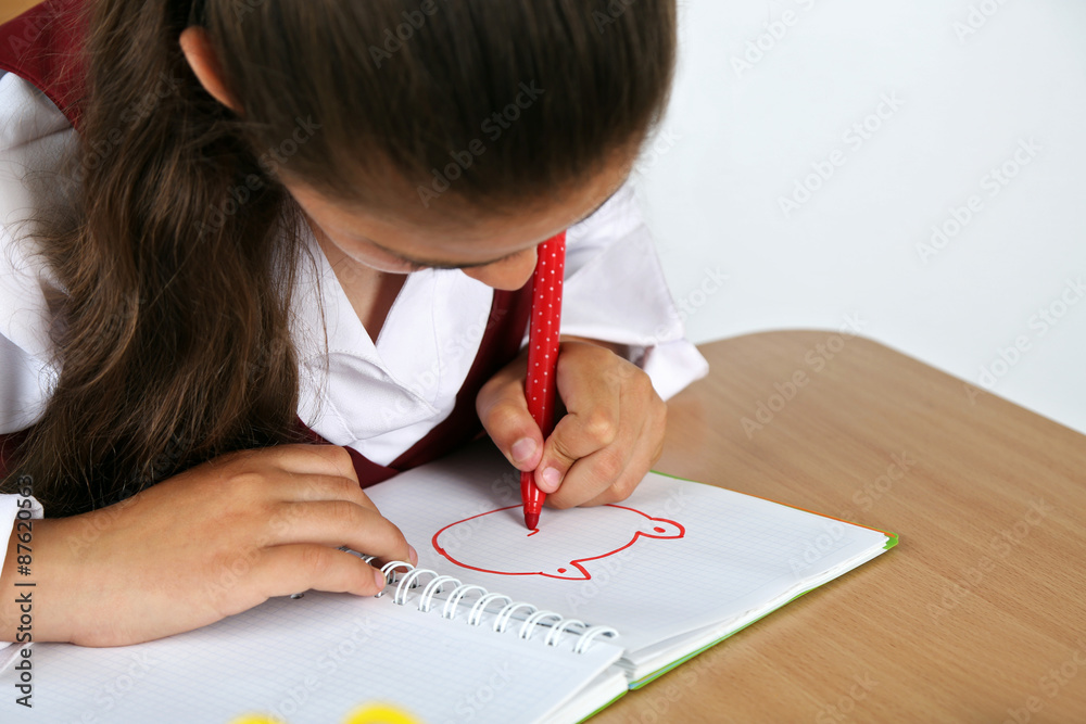 Beautiful little schoolgirl in classroom and draws in notebook Beautiful little schoolgirl in classroom and draws in notebook