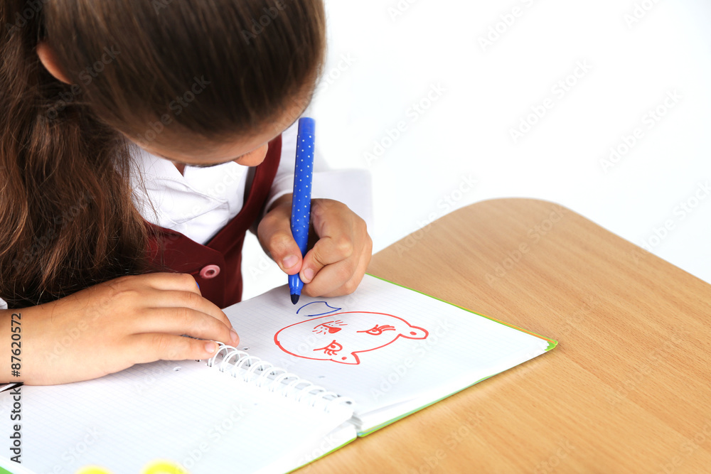 Beautiful little schoolgirl in classroom and draws in notebook Beautiful little schoolgirl in classroom and draws in notebook