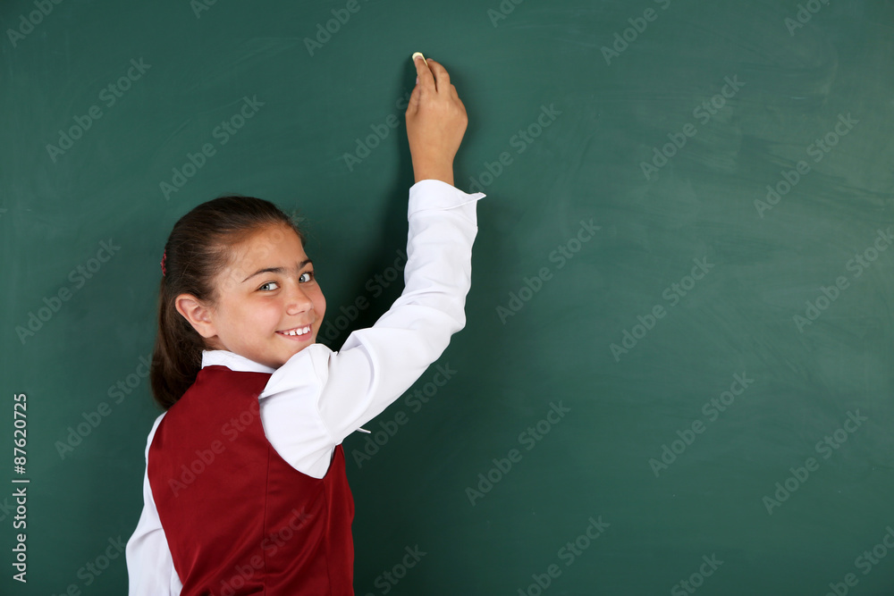 Beautiful little girl writes on blackboard in classroom