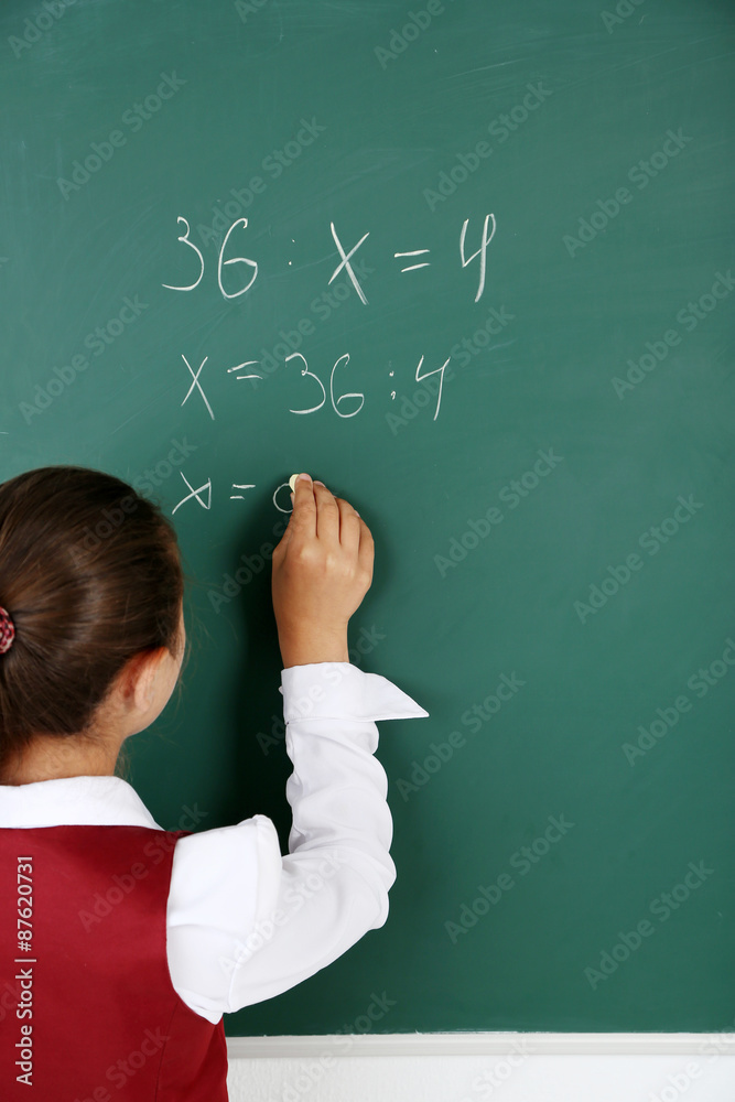 Beautiful little girl writes on blackboard in classroom Beautiful little girl writes on blackboard in classroom