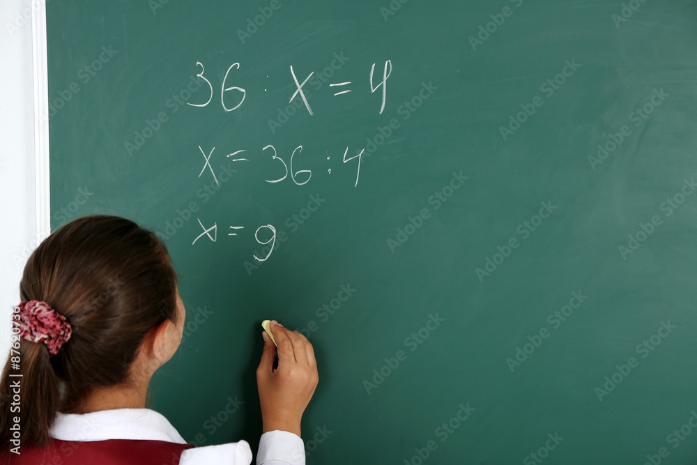 Beautiful little girl writes on blackboard in classroom Beautiful little girl writes on blackboard in classroom