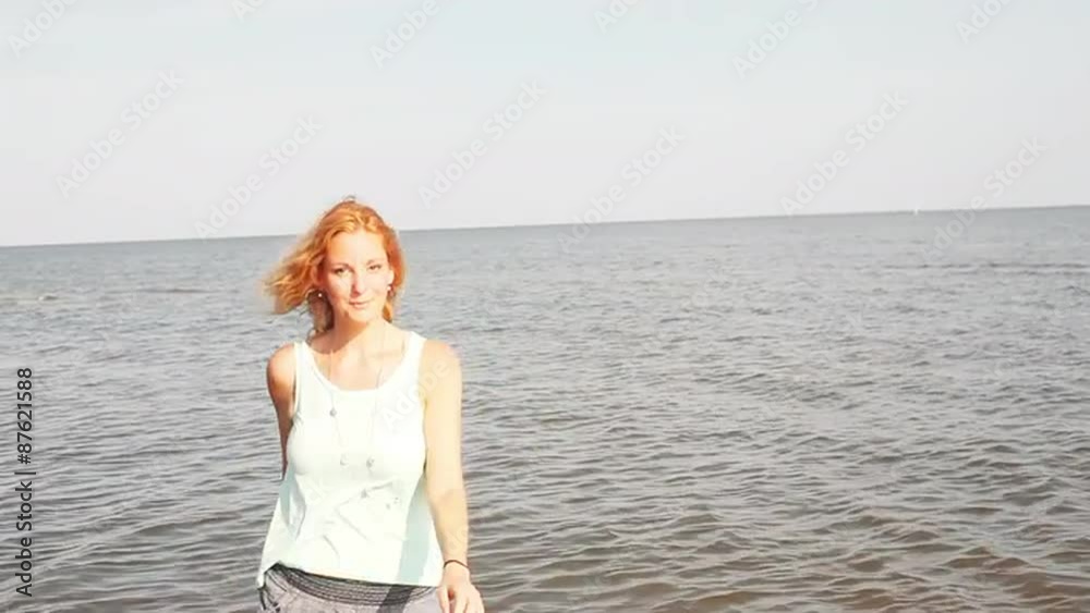 A woman looking at the camera twirls and dances in front of the water A woman looking at the camera twirls and dances in front of the water