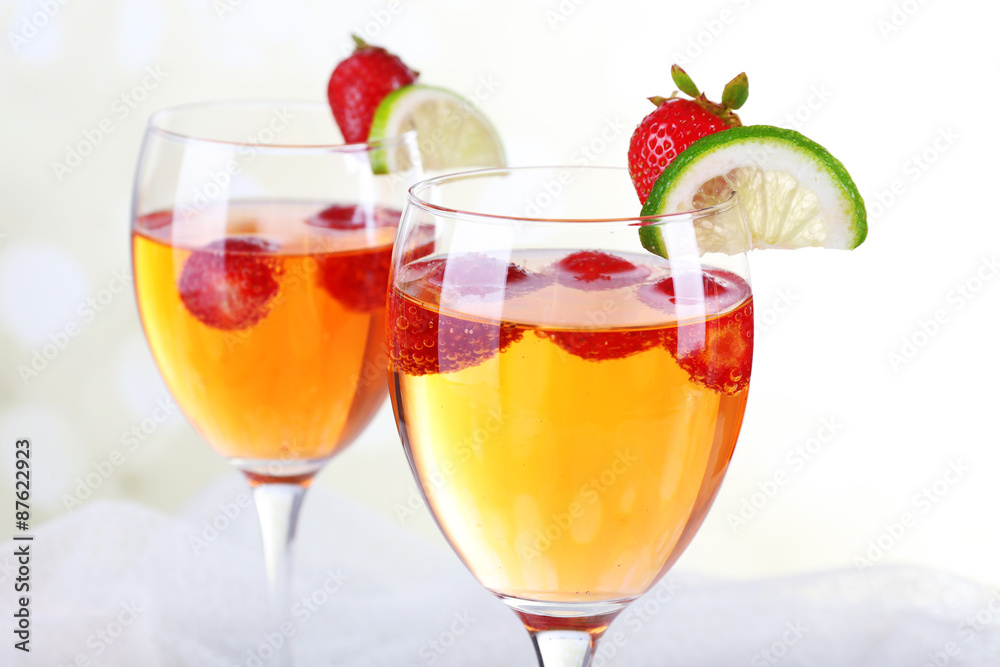 Glasses of wine with strawberries and slice of lime on light background