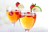 Glasses of wine with strawberries and slice of lime on light background