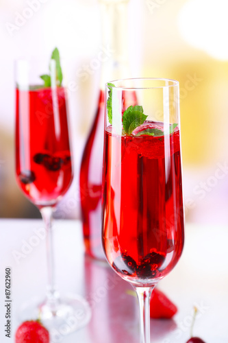 Glass of champagne with berries on light blurred background