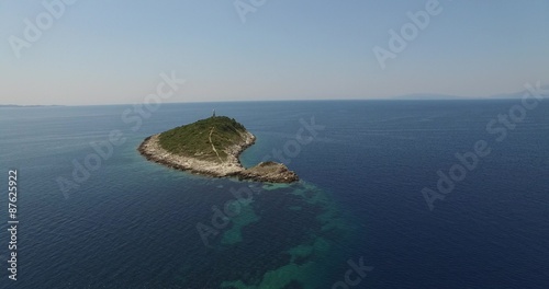Escena aérea con dron de pequeña isla con un faro en el extremo. Cámara se acerca a la isla, cambia ángulo de visión. Costa dálmata, mar Adriático. Croacia. photo