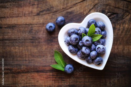Fresh ripe garden blueberries in a white heart shape bowl on dark rustic wooden table. with copy space for your text