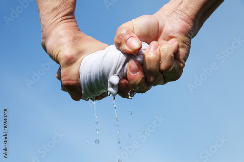 Hands squeeze wet fabric against blue sky. photo