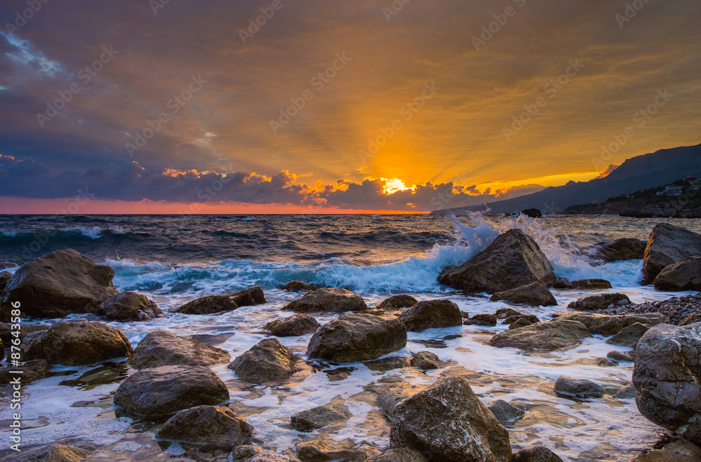 Waves break about stones at sunrise over the sea
