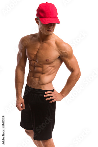 Muscular man in sport shorts posing in red cap. Three quarter length studio shot isolated on white.