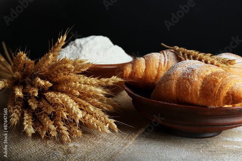 Fresh croissants with flour on wooden table on black background