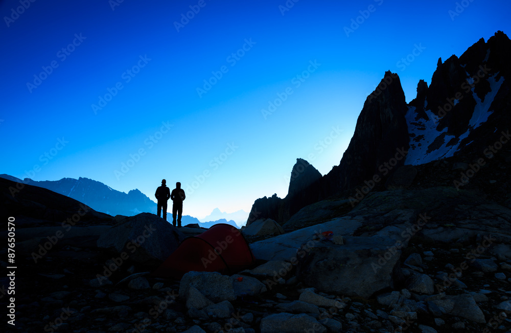 Silhouette of a couple enjoying the mountains from their campsite just before sunrise.
