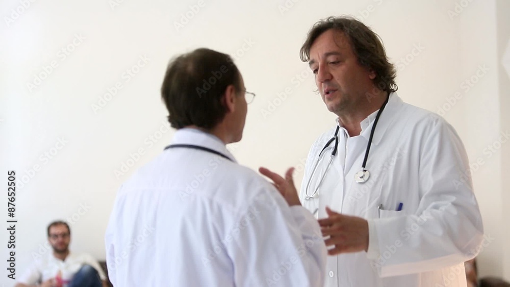 Two male doctors are discussing. On background, out of focused people in waiting room Two male doctors are discussing. On background, out of focused people in waiting room