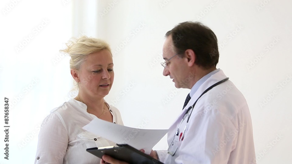 Worried blonde woman receiving prescriptions from her doctor, showing her papers results on clipboard Worried blonde woman receiving prescriptions from her doctor, showing her papers results on clipboard