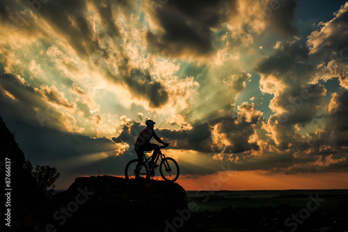 Silhouette of a biker and bicycle on sky background.