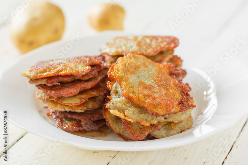 potato fritters/ hash browns with a golden crust in a white ceramic plate and crude potatoes on a table