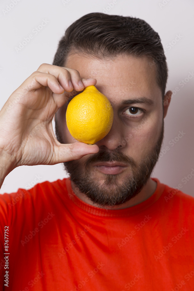 Vegetarian man holding a lemon in front of the eye Vegetarian man holding a lemon in front of the eye