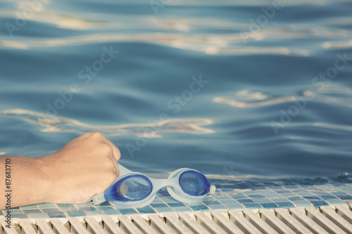 Hand holding goggles at the pool edge