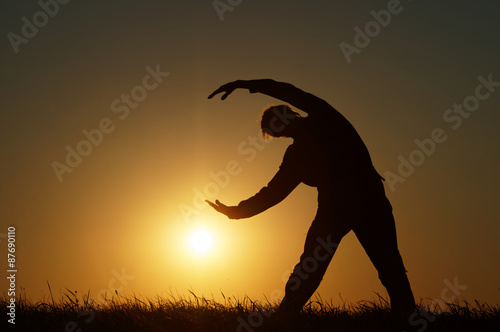 Fototapeta Naklejka Na Ścianę i Meble -  Silhouette of a man with a bow to the side on a grassy horizon of the setting sun.