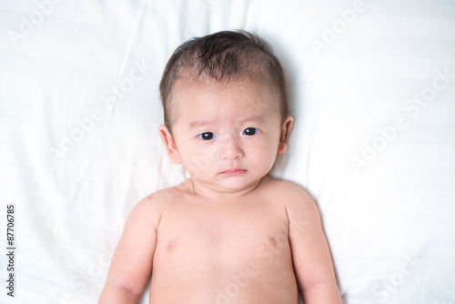 Cute Asian baby lying on a white pillow, on bed
