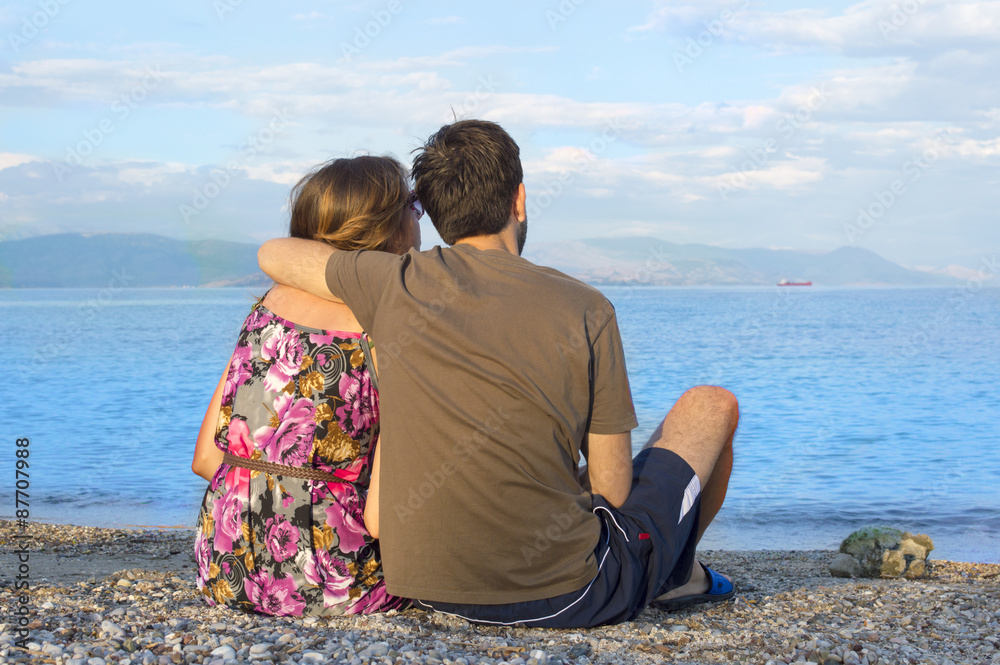 Young couple sitting together on a rocky beach and looking at th