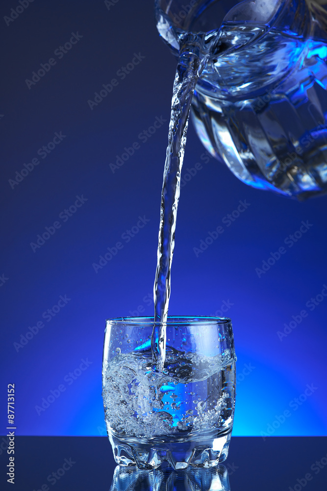 Jug water poured into a glass, splash, blue background, refreshing