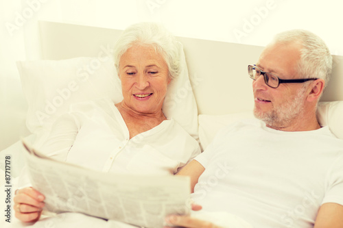 happy senior couple with newspaper in bed