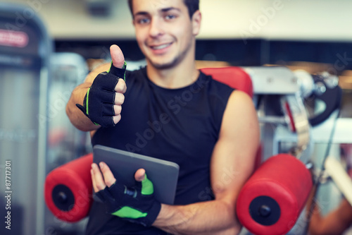 young man with tablet pc showing thumbs up in gym