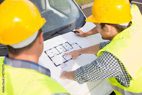 close up of builders with blueprint on car hood