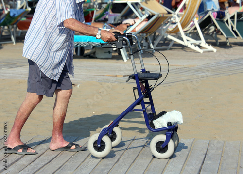 senior man walking with Walker on the beach in summer