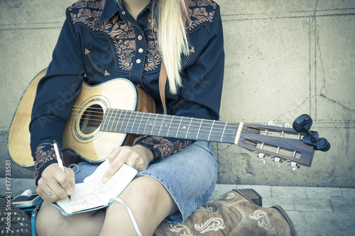 Momentos de inspiración. Chica rubia componiendo una canción sentada en el suelo de la calle. Joven músico con su guitarra.  photo
