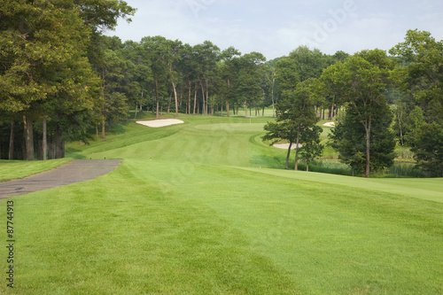 Golf fairway lined with trees leading to green and sand traps
