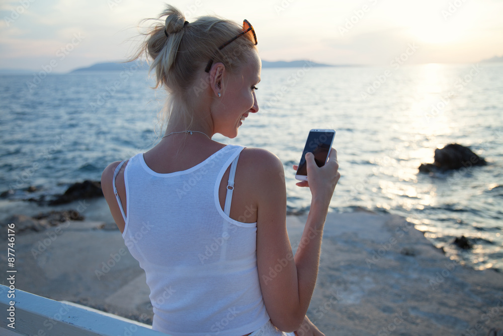 Blonde woman using cellphone on vacation.
