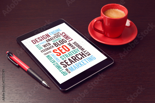 Digital tablet with SEO words and coffee cup on office desk