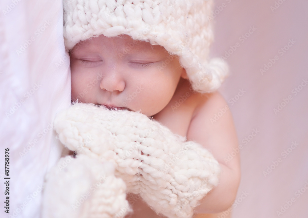 Sleeping baby wearing knitted mittens and hat in room. Bed time. Childhood. Sleeping baby wearing knitted mittens and hat in room. Bed time. Childhood.
