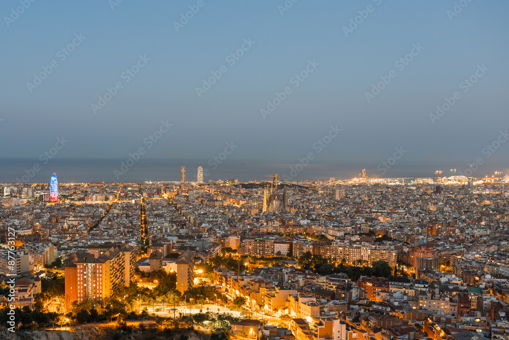 Top view and night photography of an illuminated Barcelona. The panorama shows the famous Sagrada Familia, the illuminated Torre Agbar and the Towers of the Port Olimpic until the harbor