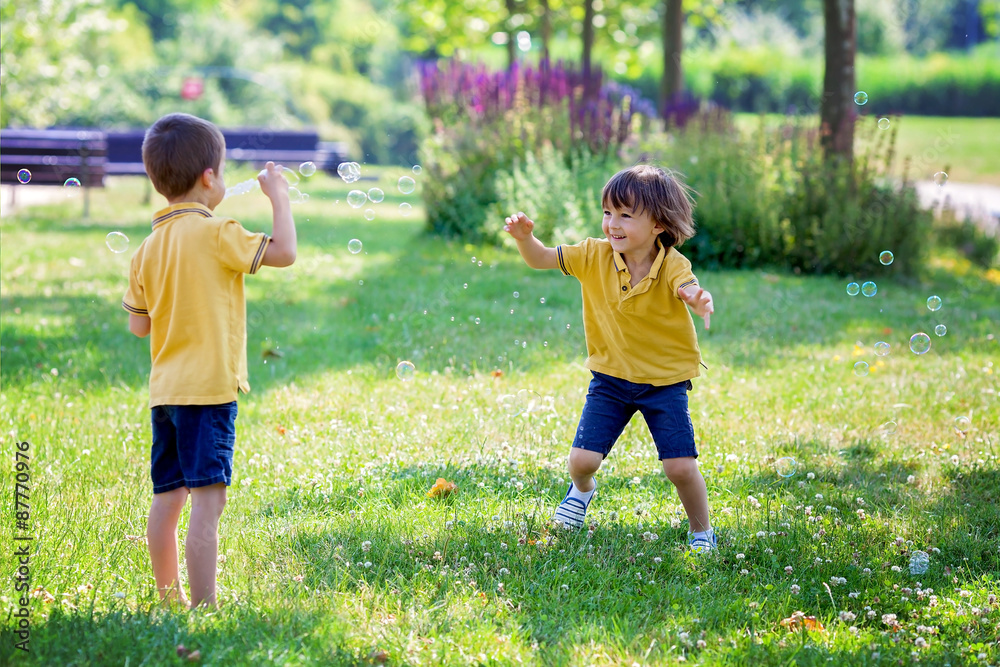 Obraz premium Two children in the park blowing and chasing soap bubbles and ha