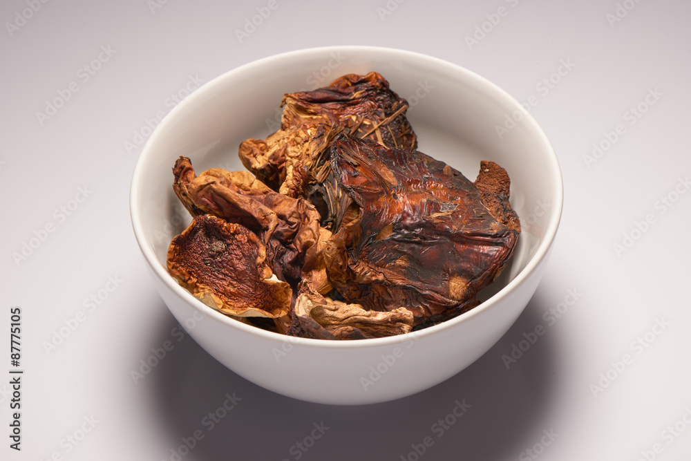 Dried mushrooms in white ceramic bowl on white background