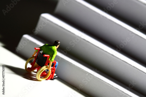 Miniature man wheelchair access concept.
Miniature scale model figure of a disabled man at the bottom of stairs.  Access issues concept. photo