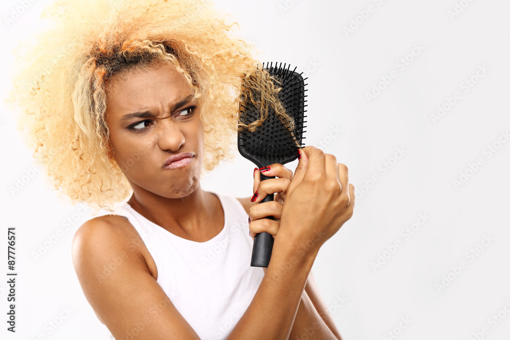 Fototapeta premium Rozczesywanie włosów. Ciemnoskóra młoda kobieta rozczesuje włosy szczotką