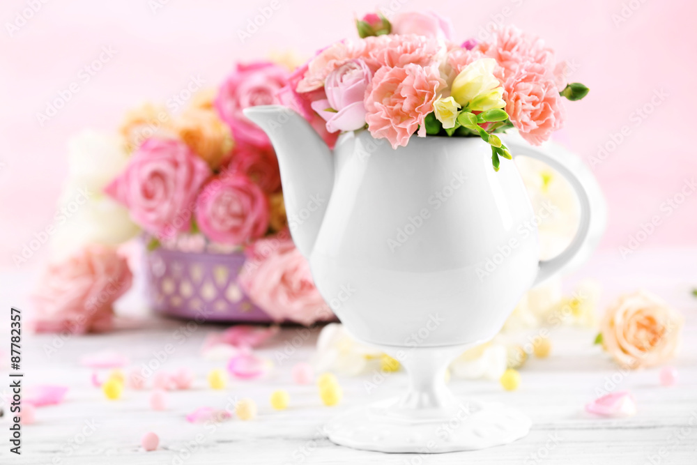Composition with beautiful spring flowers in teapot on light pink background