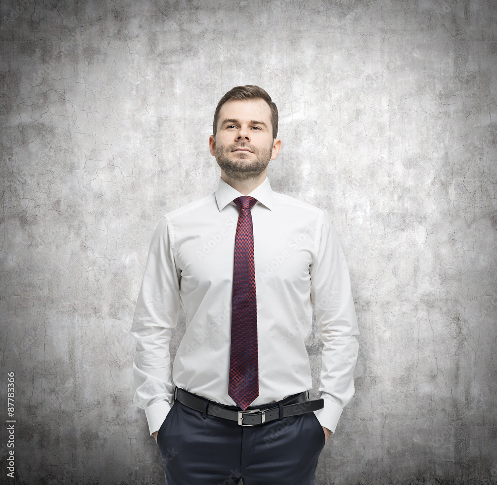 Confident businessman with hands in pockets. Concrete background.