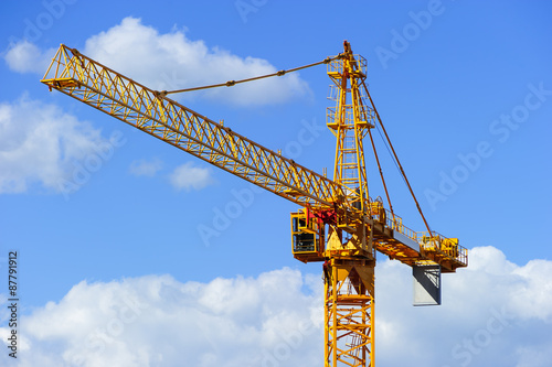 Yellow construction tower crane isolated on blue sky with white clouds background  photo