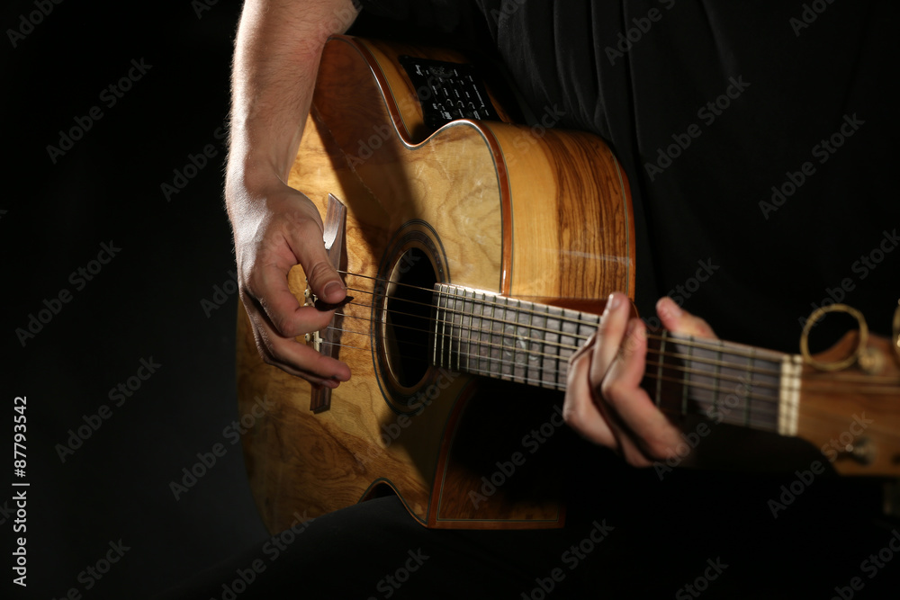 Fototapeta premium Young man playing on acoustic guitar on dark background