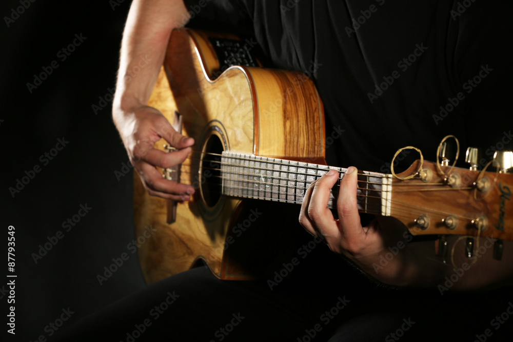 Fototapeta premium Young man playing on acoustic guitar on dark background