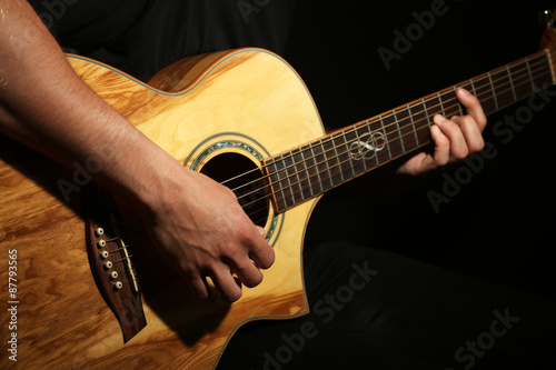 Young man playing on acoustic guitar on dark background