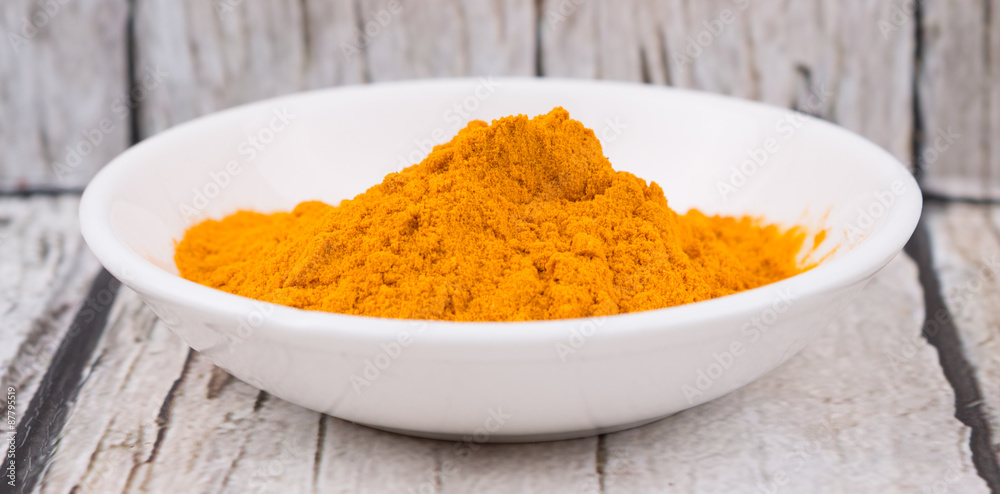 Turmeric powder in white bowl over rustic wooden background Turmeric powder in white bowl over rustic wooden background